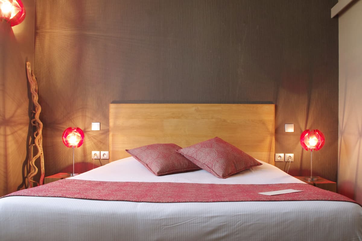 Een net opgemaakt bed met twee kussens, een houten hoofdbord en twee bedlampjes.