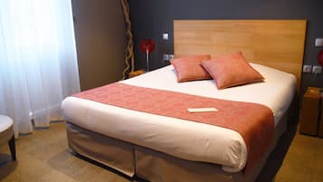 Una cama bien hecha con cabecera de madera, una colcha roja y dos almohadas a juego.