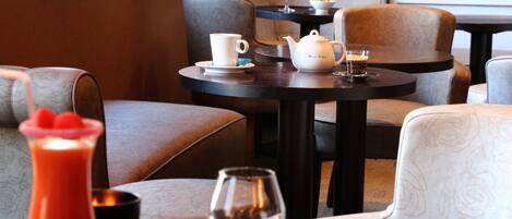 Un comedor con asientos acolchados, una mesa con tetera, tazas y vasos, y un plato de comida.