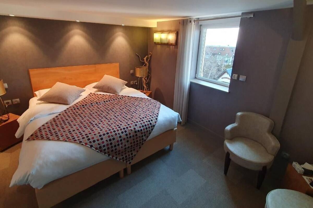 Een hotelkamer met een groot bed, een nachtkastje, een lamp, een stoel en een raam.