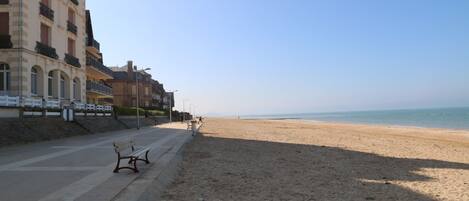 A beach with a bench and a building with balconies.