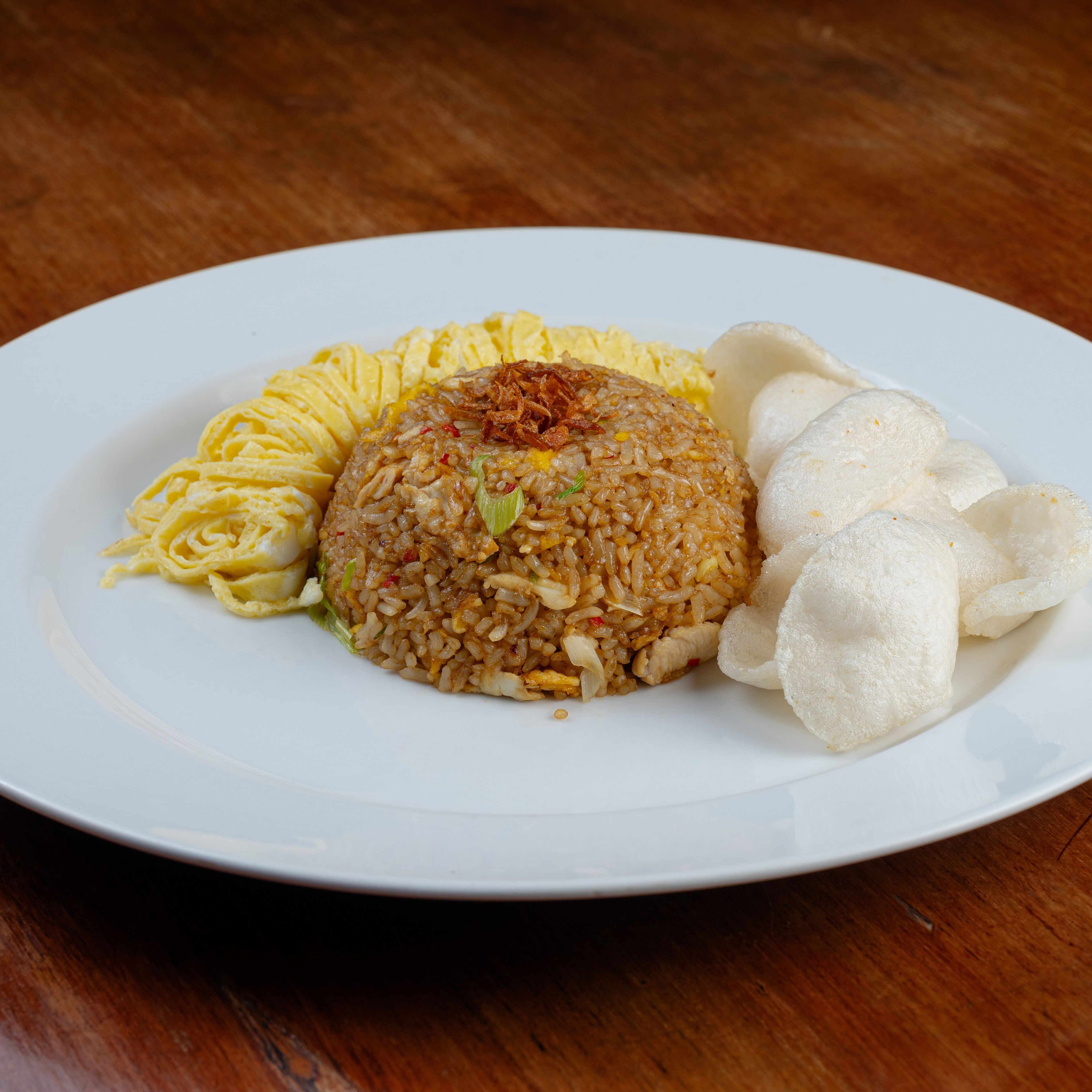 A plate of fried rice with scrambled eggs, fried onions, and a side of white rice cakes on a white plate.