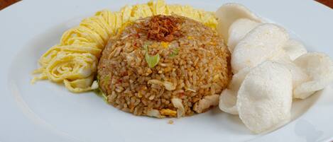 A plate of fried rice with scrambled eggs, fried onions, and a side of white rice cakes on a white plate.
