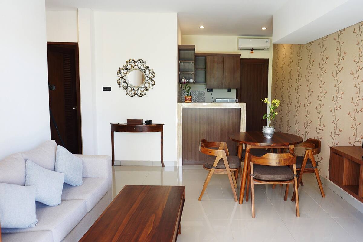 Una sala de estar moderna con un sofá, una mesa de centro, una mesa de comedor con sillas, un televisor y una cocina al fondo.