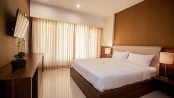 A modern hotel room with a large bed, a wooden desk, a flat-screen TV mounted on the wall, and a potted plant.