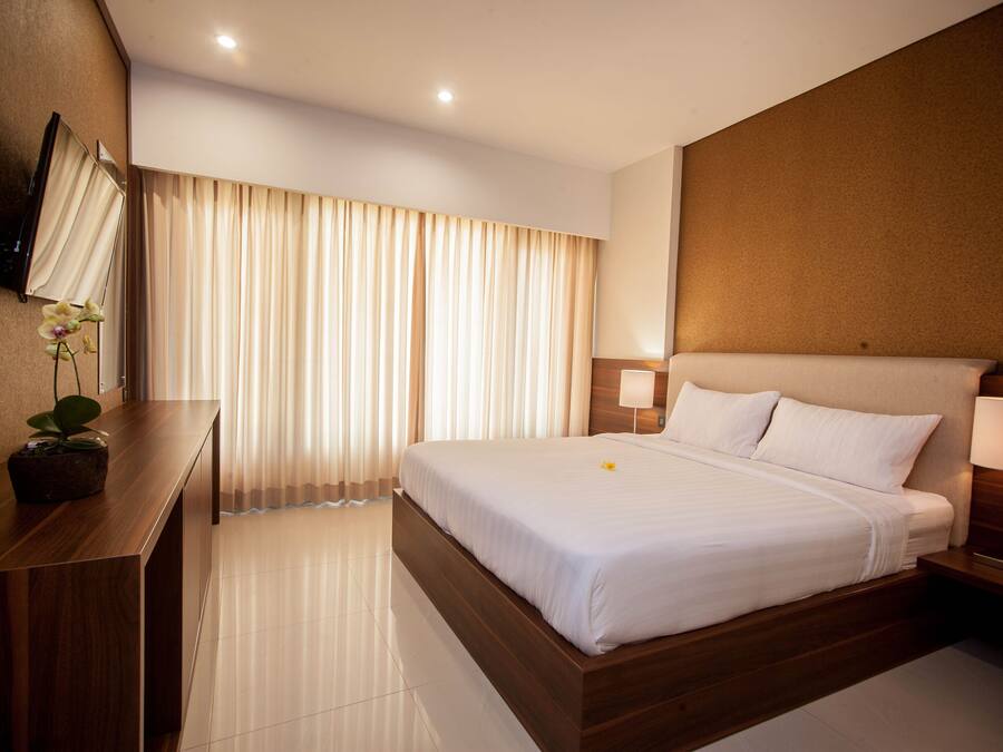 A modern hotel room with a large bed, a wooden desk, a flat-screen TV mounted on the wall, and a potted plant.