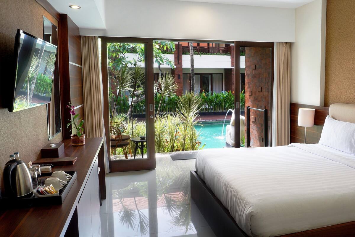 Habitación de hotel con una cama grande, televisión, escritorio con cafetera y vista a una piscina.