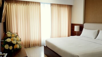 Una camera d'albergo con un letto grande, un comodino, una lampada e un bouquet di fiori.