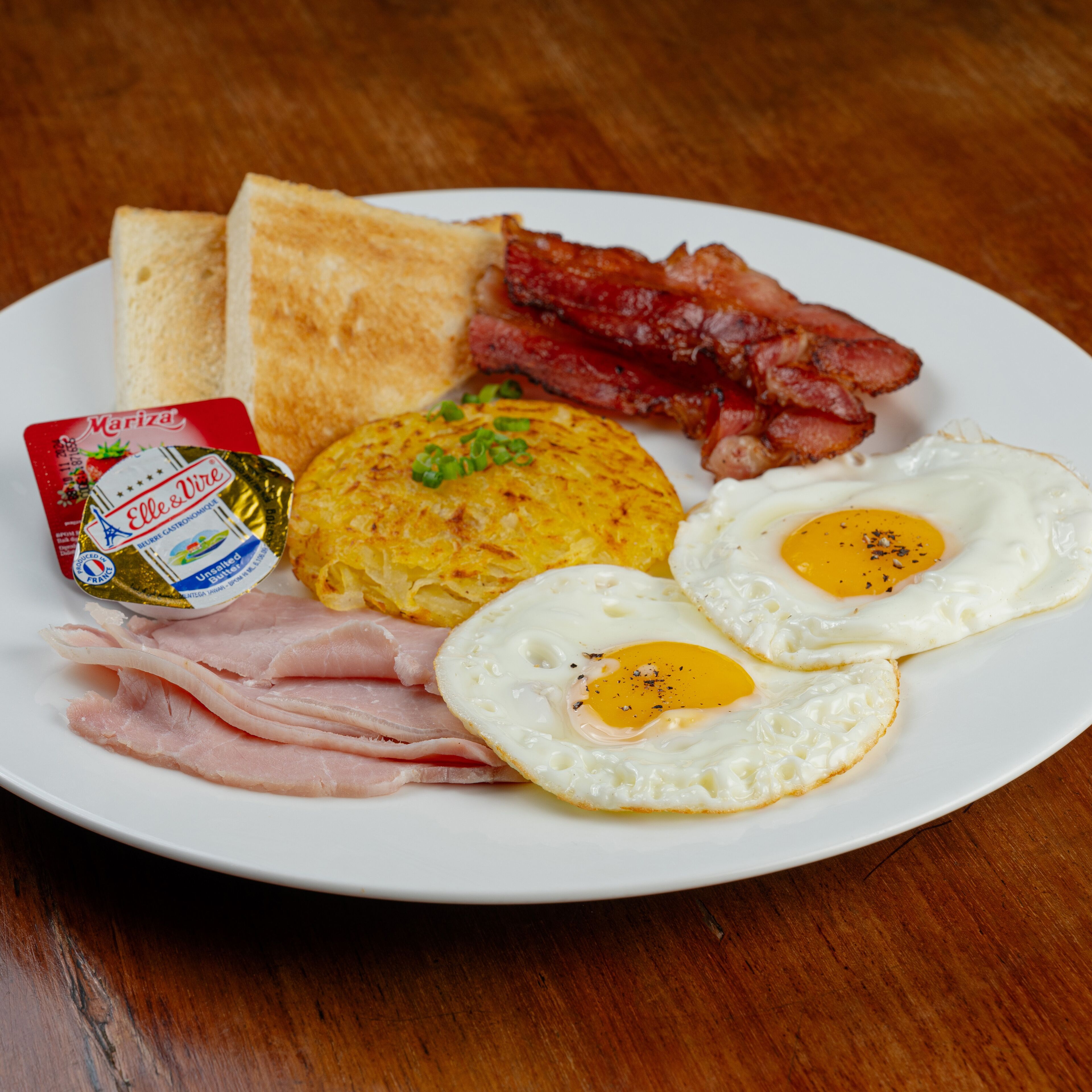A plate with toast, bacon, eggs, ham, and a butter packet.