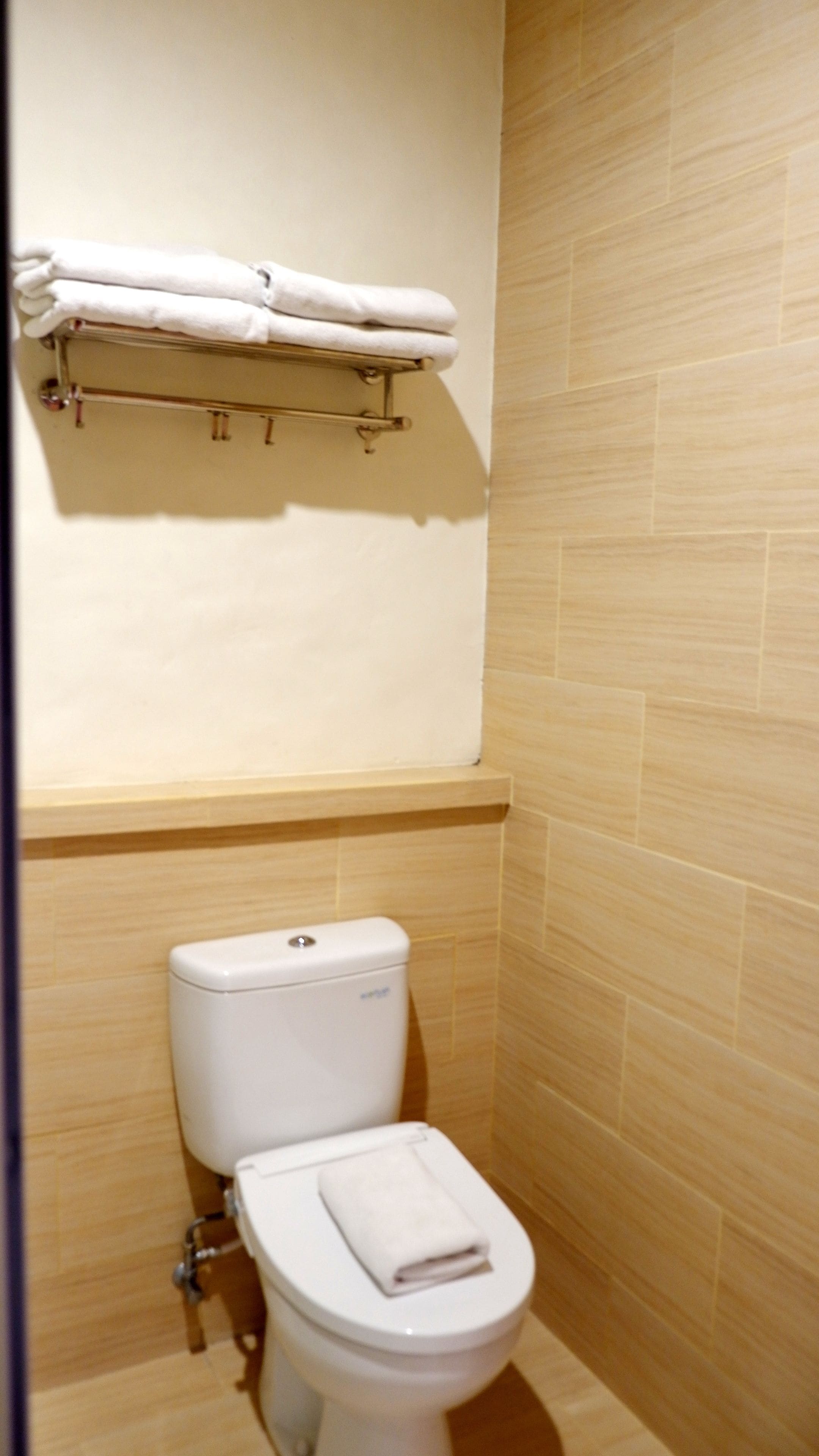 Un baño con inodoro, un perchero con toallas dobladas y revestimiento de madera en las paredes.