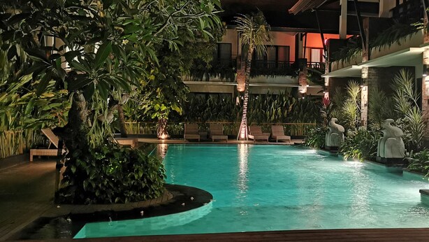 An indoor swimming pool with a waterfall feature, surrounded by lush greenery and seating areas. - Arena Living (Denpasar)