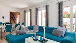 Uma sala de estar moderna com um sofá azul-turquesa, uma mesa de centro de vidro e uma área de jantar com uma mesa branca e cadeiras azul-turquesa.