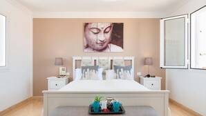Quarto com cama grande, duas mesas de cabeceira, uma obra de arte na parede e janela com vista.