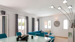 Uma sala de estar moderna com uma mesa de jantar de vidro, cadeiras cor turquesa, um sofá e um relógio de parede grande.