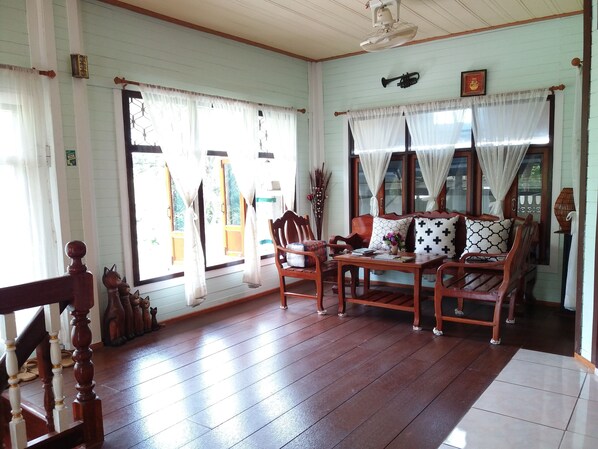 A room with wooden flooring, a sofa set, a table, and curtains. - Green Riverside Homestay (Ayutthaya)