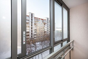 A view from a window with a metal frame and a glass door, overlooking a multi-story residential building with balconies. - Apartment Etazhydaily Ilyich-Kuznetsov (Yekaterinburg)