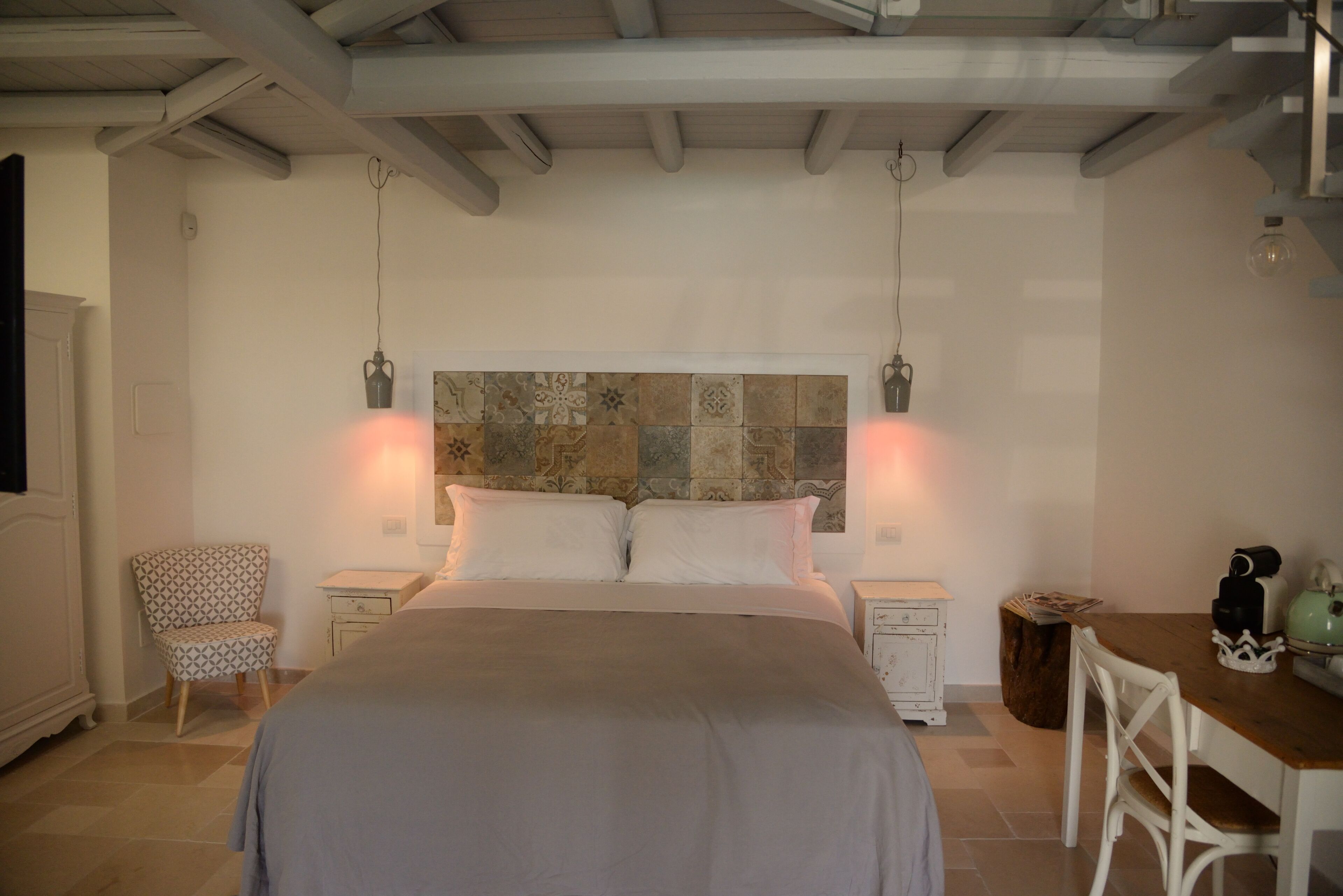 A bedroom with a bed, two bedside tables, a chair, a small table, and a decorative headboard.