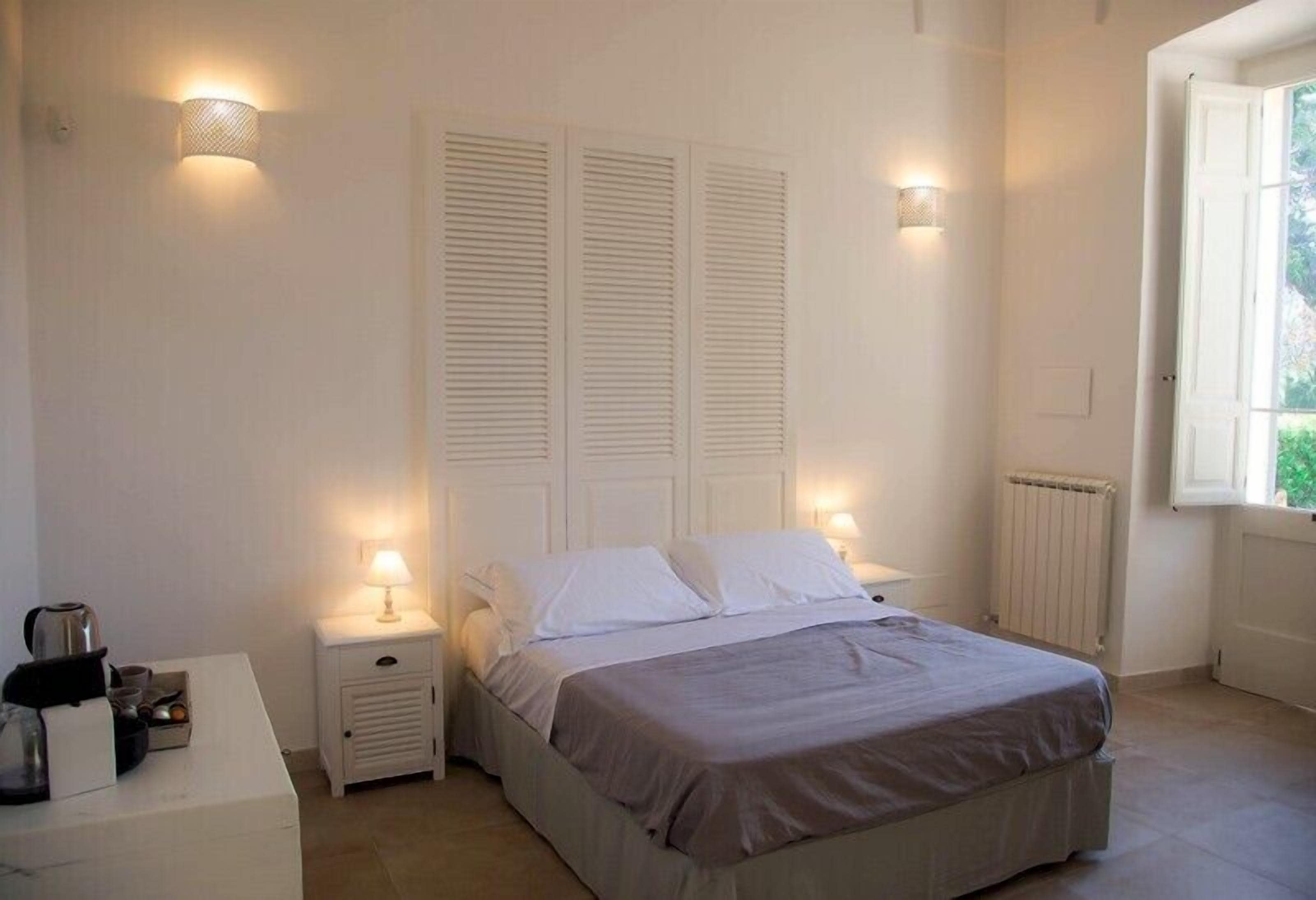 A bedroom with a bed, nightstands, a dresser, and two wall-mounted lamps.
