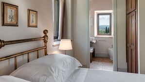 A bedroom with a bed, a bedside lamp, and a window with a view of a bathroom and outside landscape. - Frantoio - Il Casale di Villore, Poggibonsi, Siena, Tuscany (Poggibonsi)