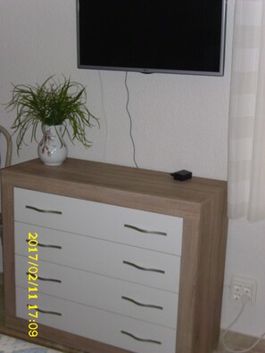 Un mueble de madera con cajones, una planta en maceta y un televisor montado en la pared.