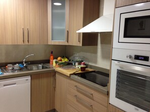 Una cocina con armarios de madera, un lavamanos de acero inoxidable, un microondas y un reloj marcando 02:59.