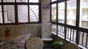 Eine Ecke eines Raumes mit einer gefliesten Wand, einem Stuhl, einem Tisch mit Topfpflanze und einem Fenster mit Blick auf Gebäude.