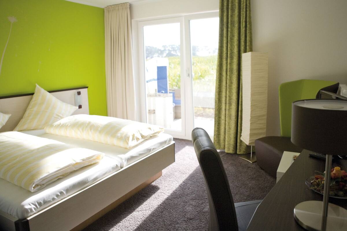A hotel room with a bed, a desk with a lamp, a chair, and a view of the outdoors through a sliding door.