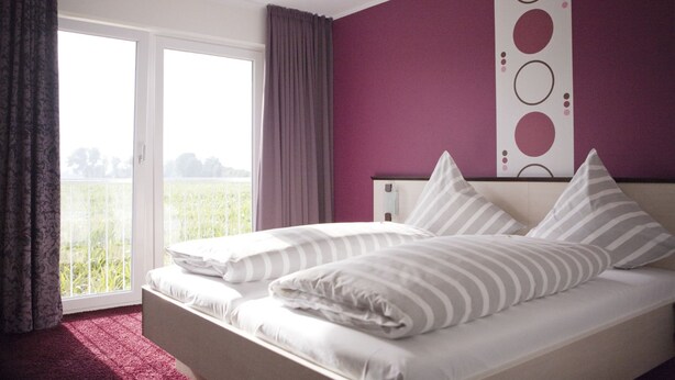 Une chambre avec un lit, une vue sur la verdure par la fenêtre et un mur de couleur violette.