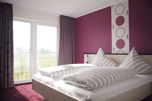 A bedroom with a bed, a view of greenery through a window, and a purple wall. - Hotel Fauna (Breiholz)