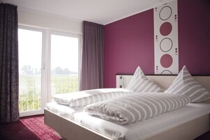 Ein Schlafzimmer mit einem Bett, Blick auf Grün hinter einem Fenster und einer violetten Wand.