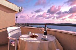 A table set with a plate of pastries, a wine glass, and a cup, overlooking a scenic view of a body of water and distant hills. - Cvita apartments (Trogir)