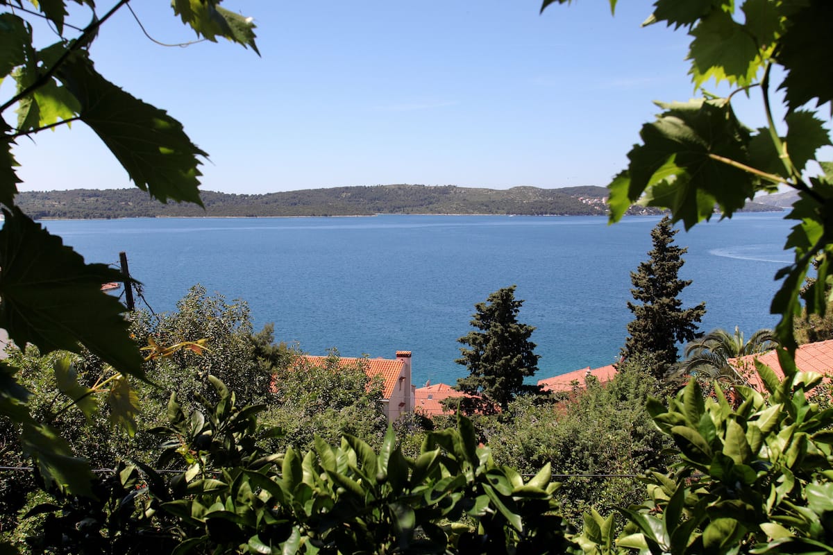 A coastal view with a clear blue sea, a distant shoreline, and surrounding greenery.