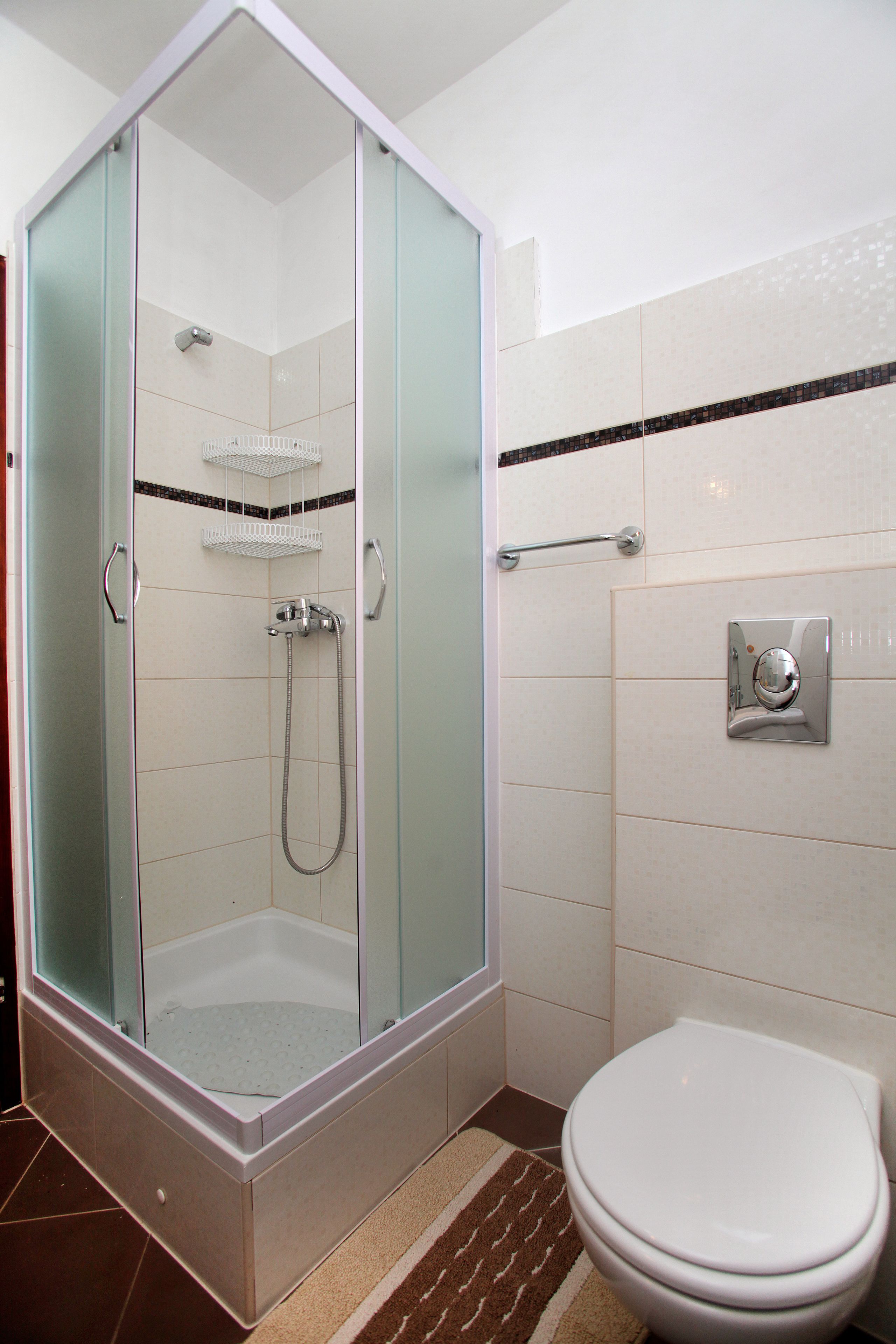 A bathroom with a glass-enclosed shower, a white toilet, and a tiled floor.