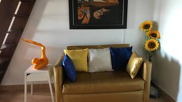 A living room with a brown leather sofa, a white side table, a framed painting, and a vase with sunflowers.