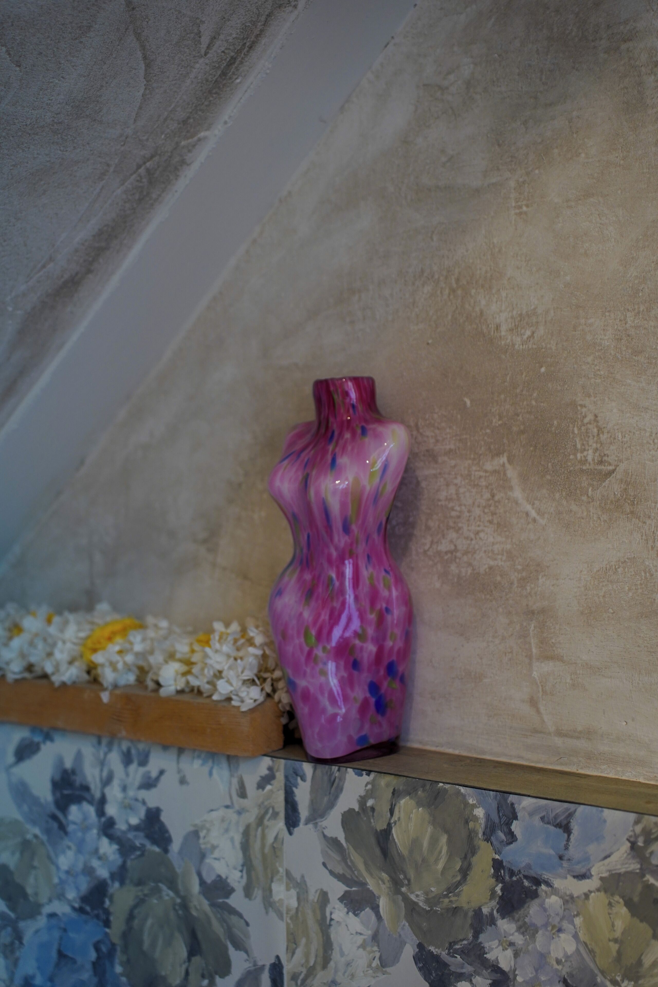 A pink vase with a floral pattern on a shelf.