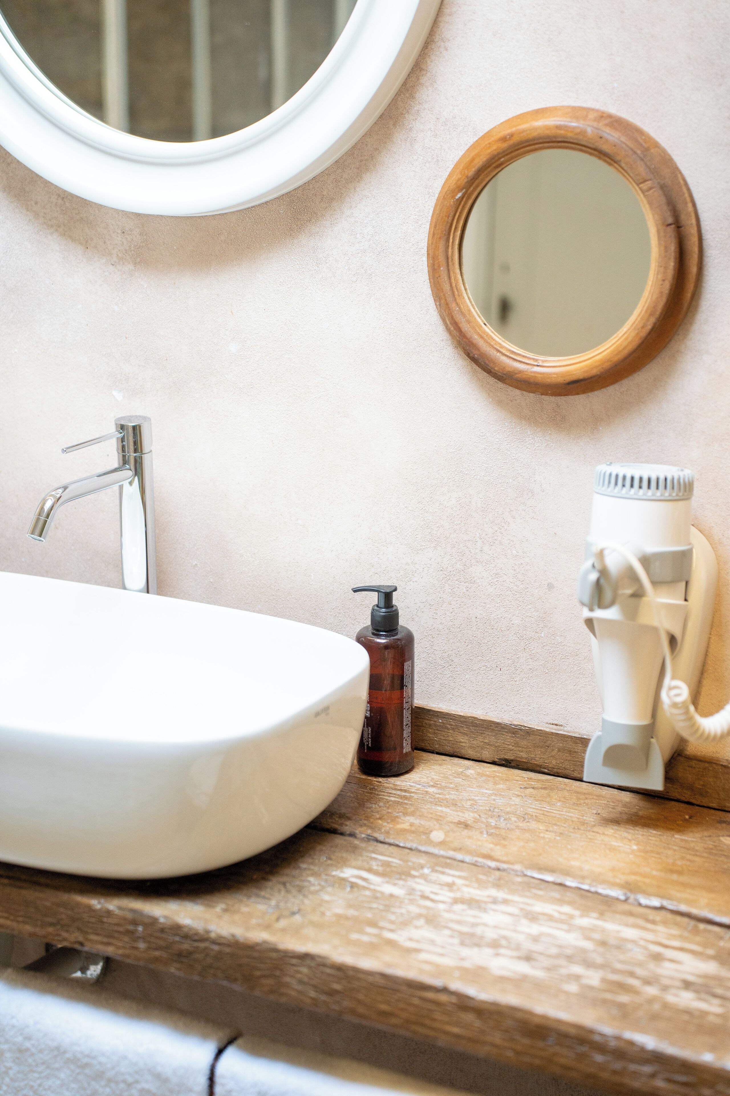 A bathroom with a white sink, a round mirror, a wooden countertop, and a hairdryer.