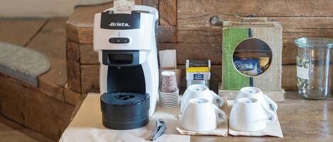 A wooden table with a coffee maker, cups, and a jar.