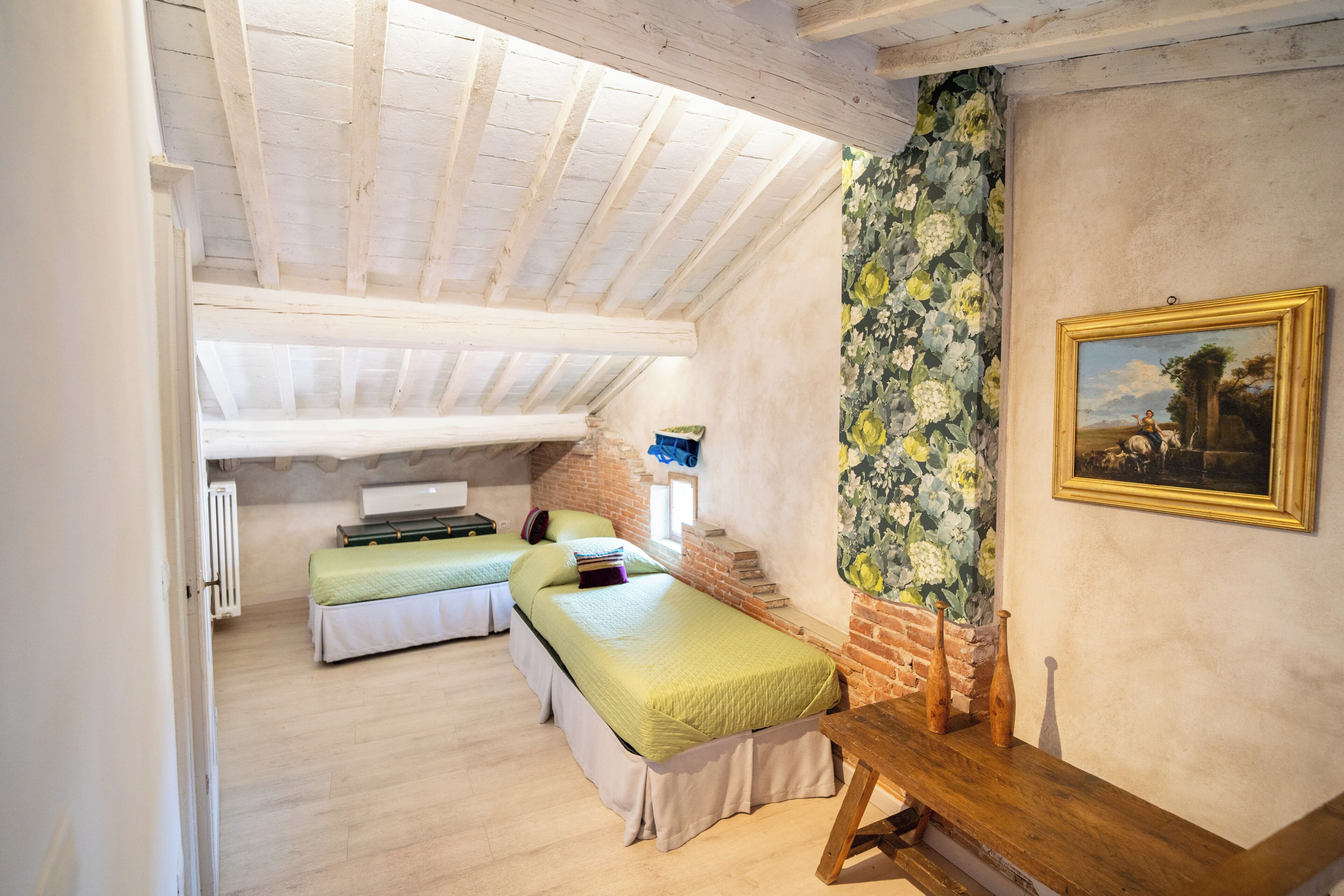 A room with two beds, a wooden table, a painting, and a brick wall.