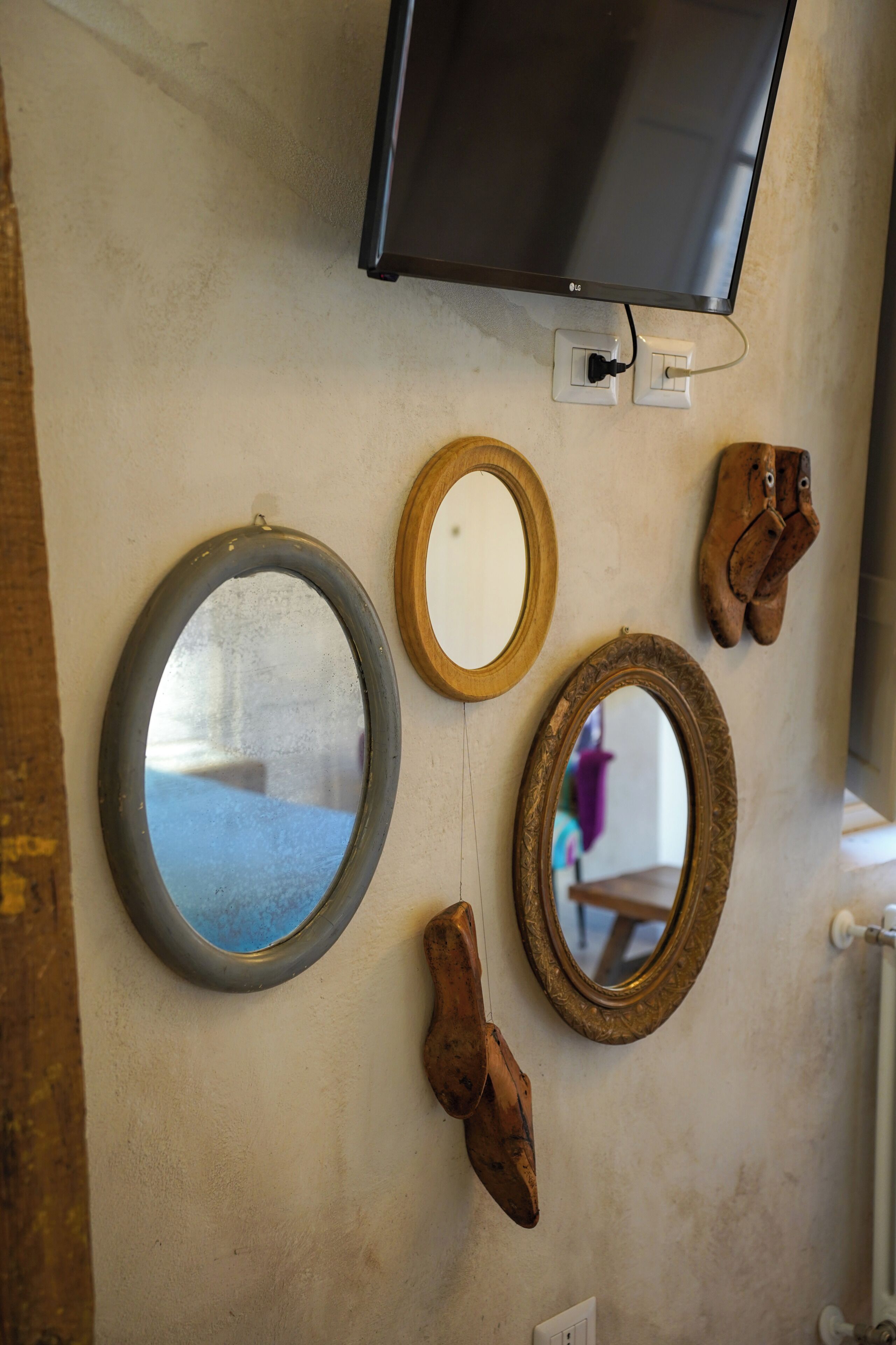 A wall with a flat-screen TV, three mirrors, and a pair of boots.