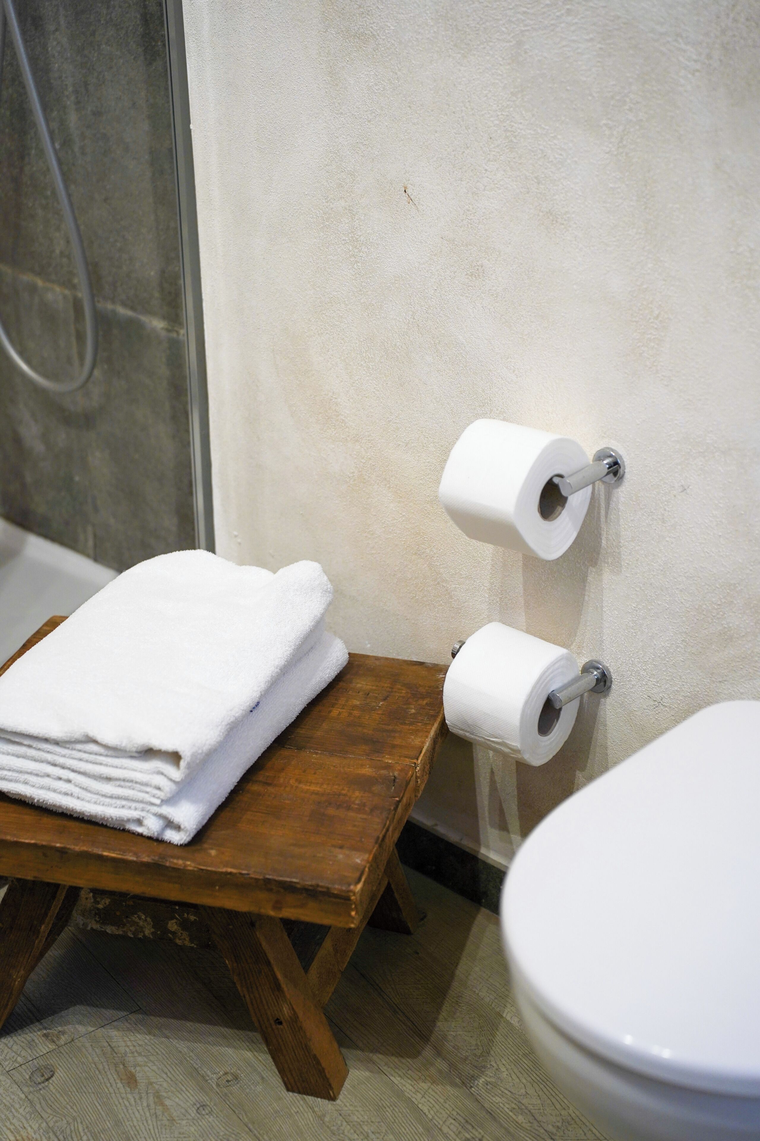 A bathroom with a wooden bench, two rolls of toilet paper, and a white toilet.