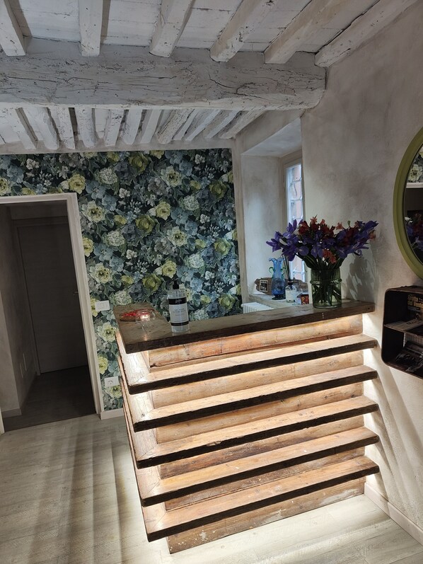 Una escalera de madera lleva a una habitación con papel tapiz floral y una pequeña mesa con un jarrón de flores.