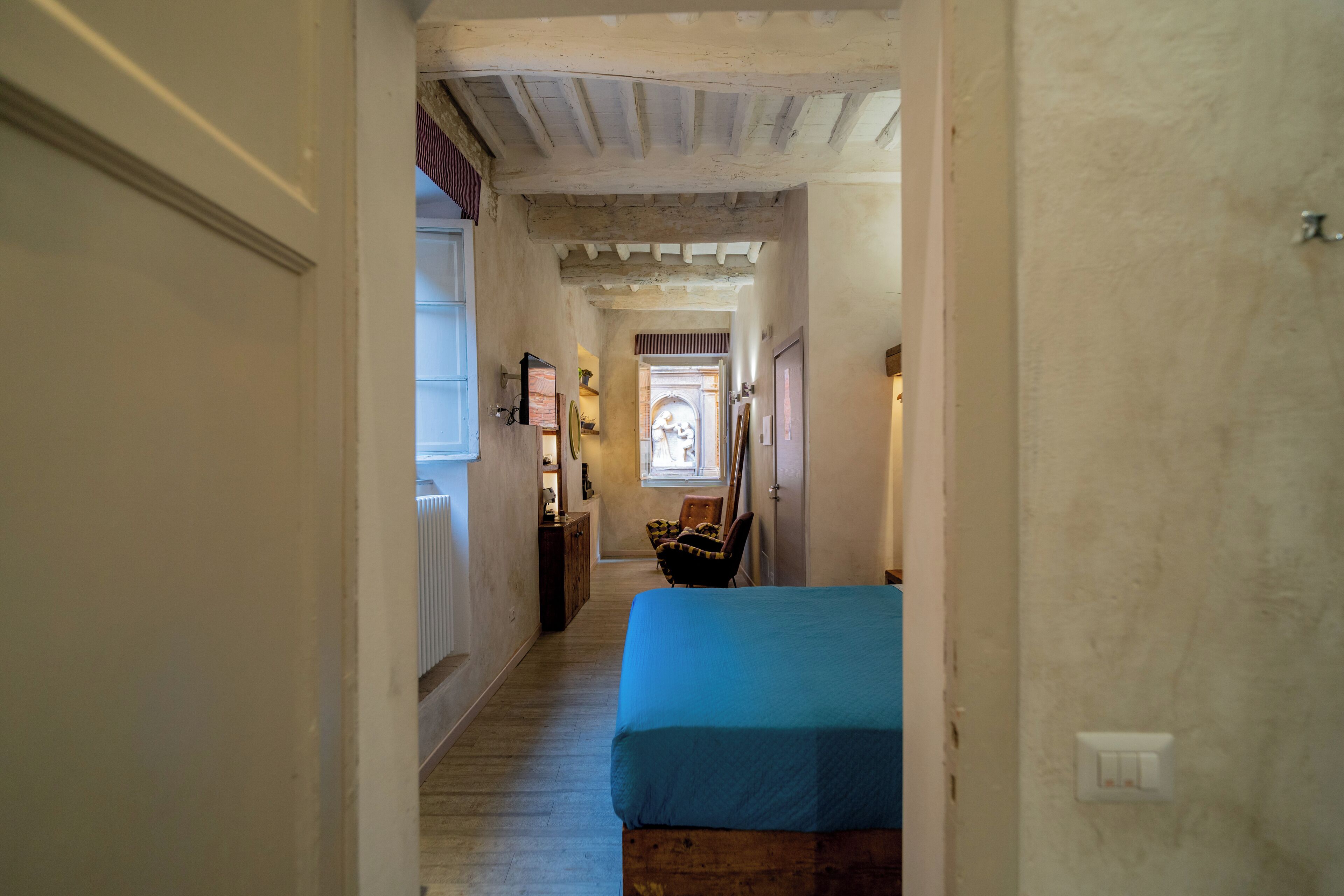 A narrow hallway with a wooden floor, a bed with a blue cover, and a chair.