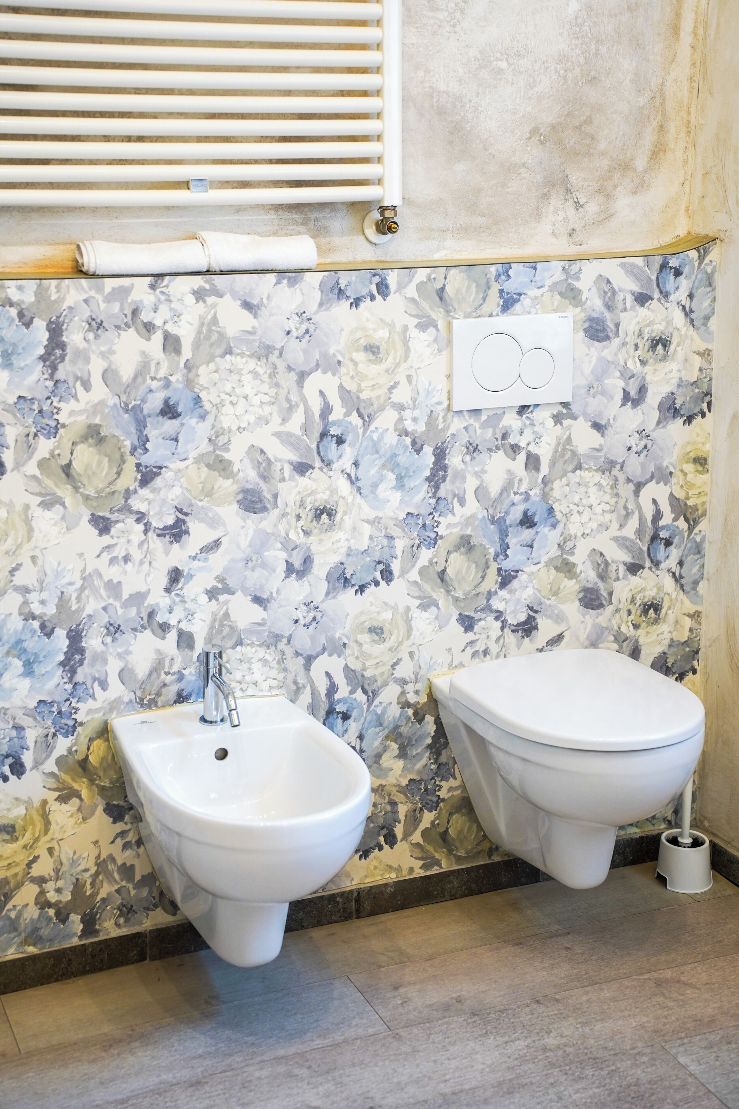 Un baño con bidé, inodoro y pared con papel tapiz floral.