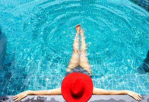 Eine Person liegt im Schwimmbecken mit ausgestreckten Beinen, trägt einen roten Hut und gestreifte Badebekleidung.