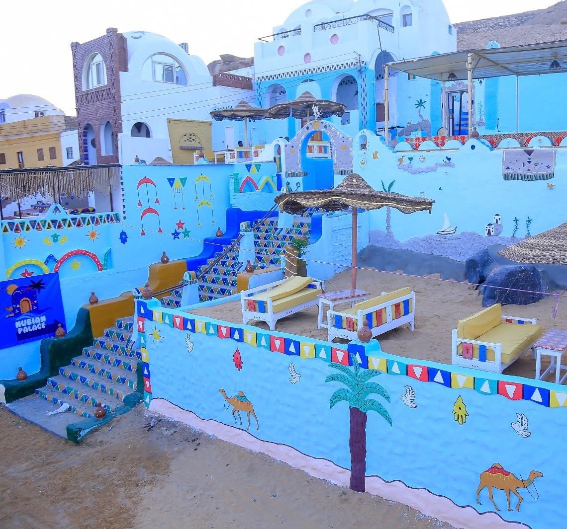 A colorful outdoor area with a palm tree, a camel, and a staircase leading to a building.