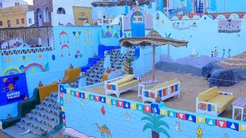 A colorful outdoor area with a palm tree, a camel, and a staircase leading to a building.
