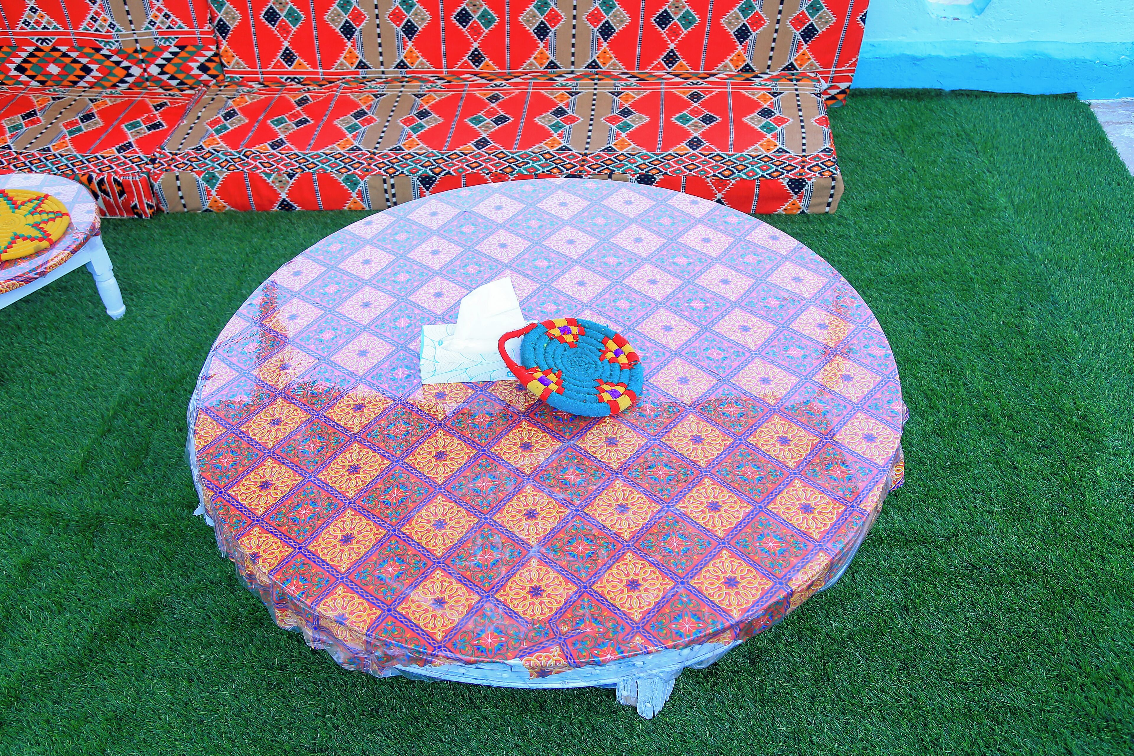 Una mesa redonda con mantel estampado, una silla blanca y un cojín de colores.