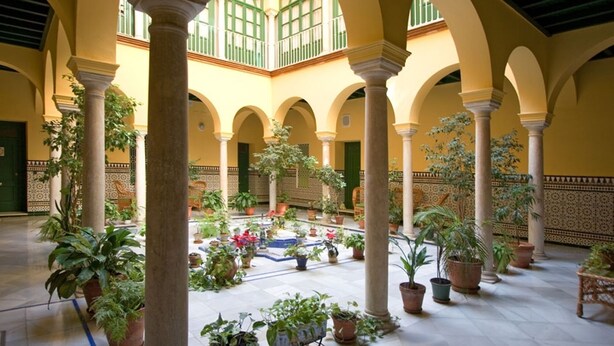 Un patio con arcos, columnas y plantas en macetas.