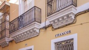 Un edificio amarillo con balcones, un cartel que dice "FRANCOS" y una puerta con la leyenda "ALQUITARA".