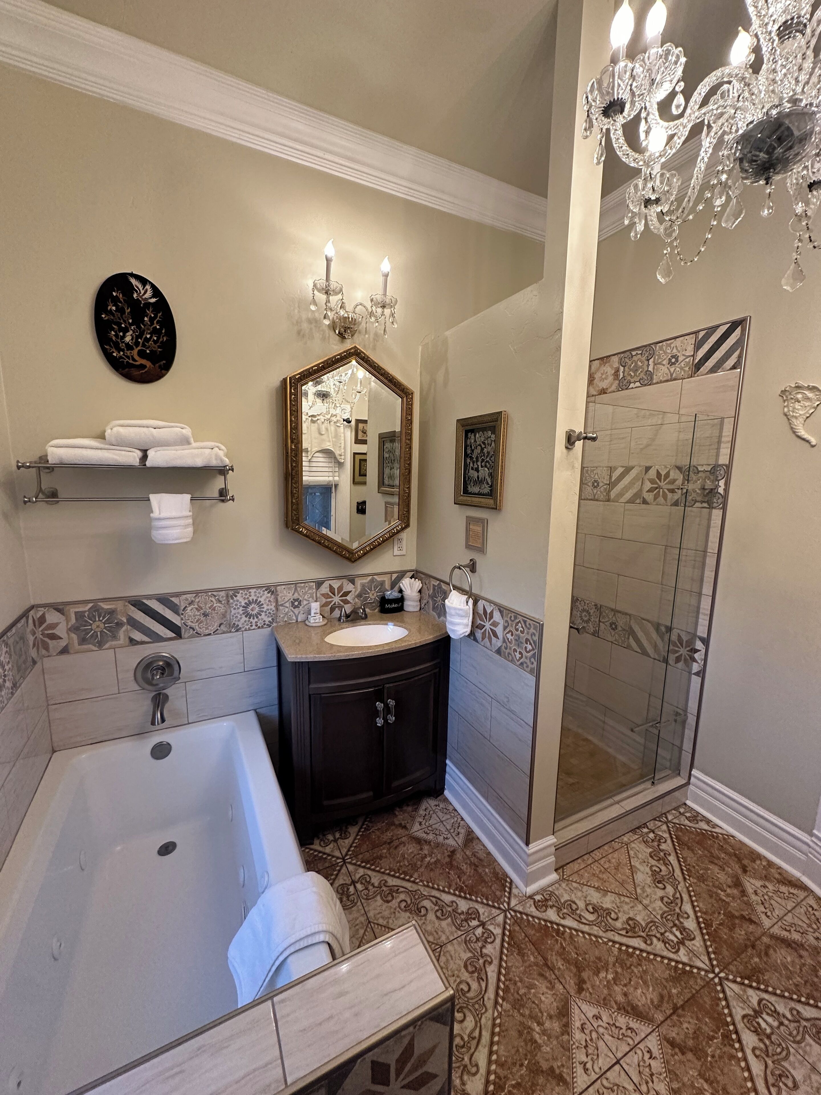 A bathroom with a large bathtub, a vanity with a sink, a shower, and a chandelier.